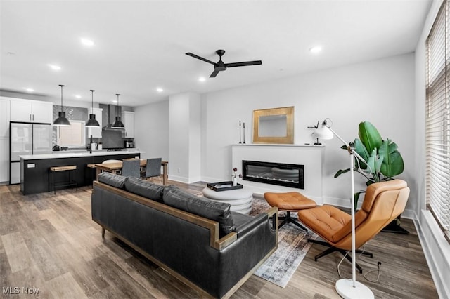 living area with light wood-type flooring, recessed lighting, baseboards, and a glass covered fireplace