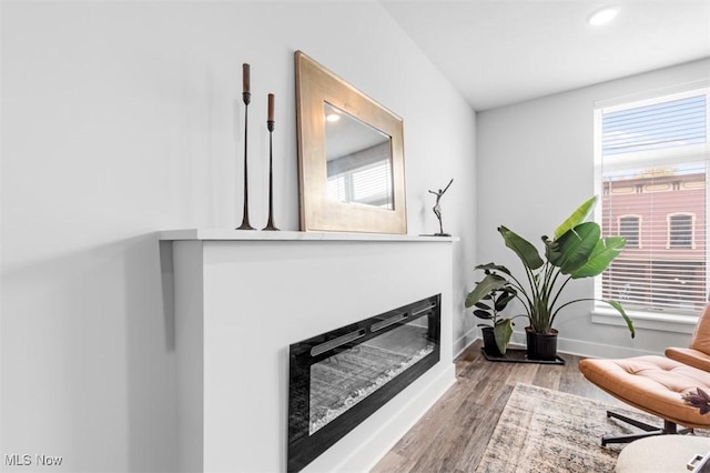 interior space with a glass covered fireplace, recessed lighting, baseboards, and wood finished floors