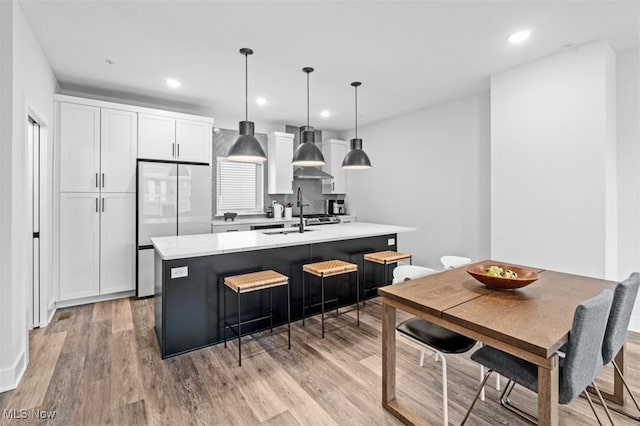 kitchen featuring a sink, light countertops, light wood finished floors, an island with sink, and stainless steel fridge