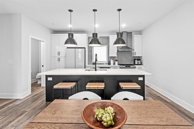 kitchen featuring decorative backsplash, white cabinets, an island with sink, wood finished floors, and a sink