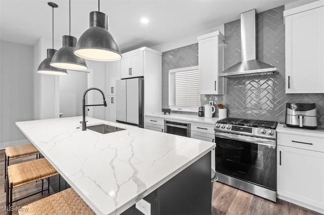 kitchen with stainless steel gas stove, wall chimney exhaust hood, freestanding refrigerator, a kitchen island with sink, and a sink