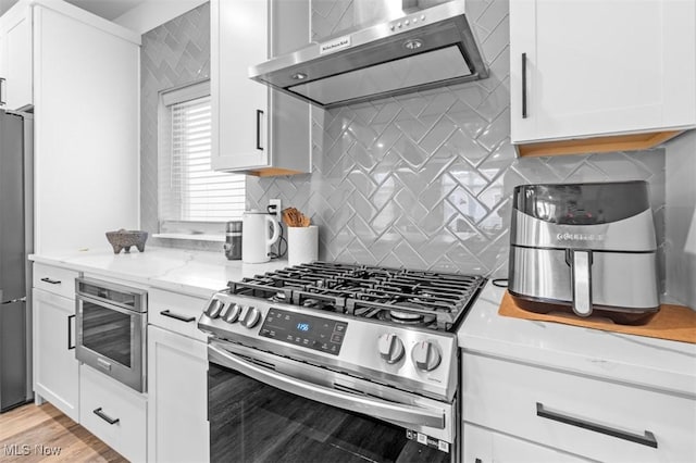 kitchen featuring light stone counters, stainless steel appliances, backsplash, white cabinetry, and extractor fan