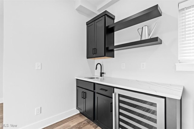 bar featuring beverage cooler, light wood-type flooring, a sink, and baseboards