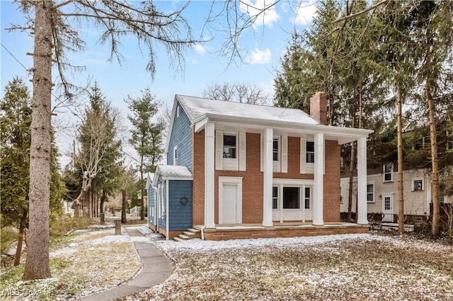 greek revival inspired property with covered porch, brick siding, and a chimney