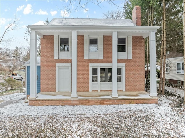 view of front facade with brick siding, a chimney, and a porch