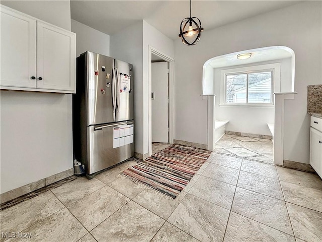 kitchen with light tile patterned floors, baseboards, white cabinets, freestanding refrigerator, and decorative light fixtures