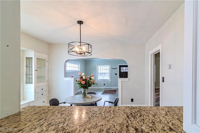 kitchen featuring stone counters, arched walkways, hanging light fixtures, a textured ceiling, and a chandelier