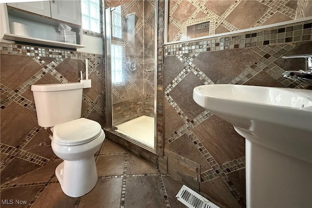 bathroom with toilet, a shower stall, visible vents, and tile walls