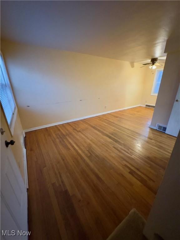 empty room featuring a ceiling fan, wood finished floors, visible vents, and baseboards