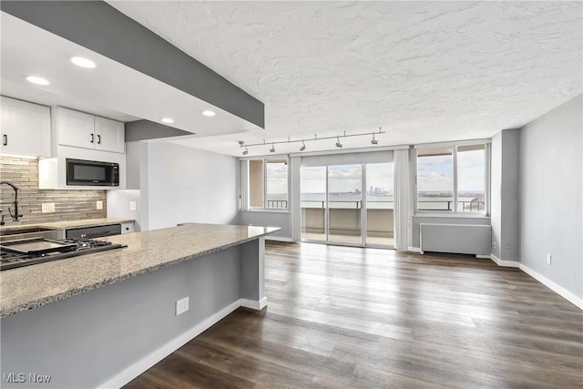 kitchen featuring tasteful backsplash, dark wood-style flooring, black microwave, and light stone counters