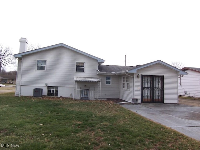 back of property with a chimney, central AC unit, and a yard