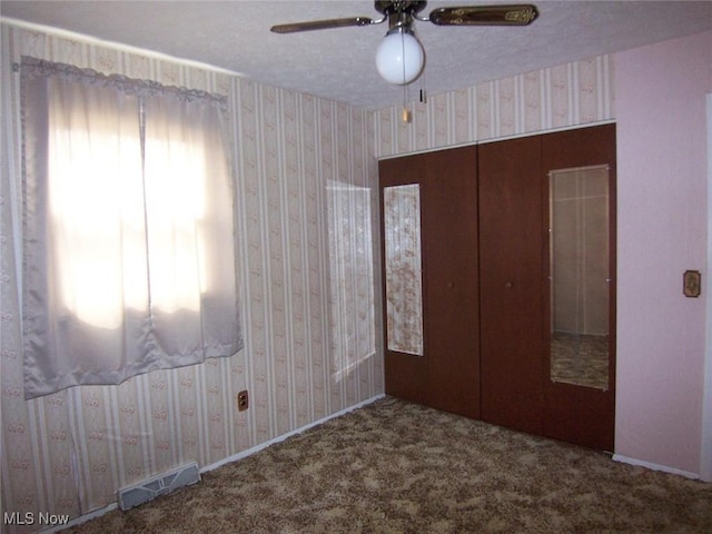 unfurnished bedroom featuring wallpapered walls, carpet, visible vents, and a ceiling fan