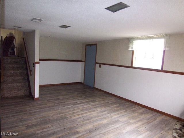 empty room with stairs, a textured ceiling, wood finished floors, and baseboards