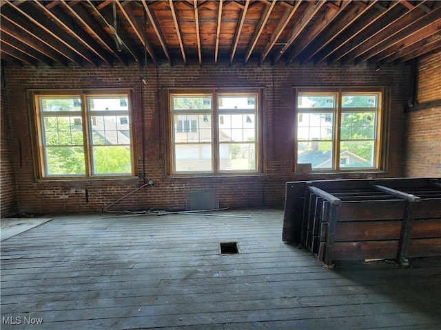 miscellaneous room with wood-type flooring, plenty of natural light, and brick wall