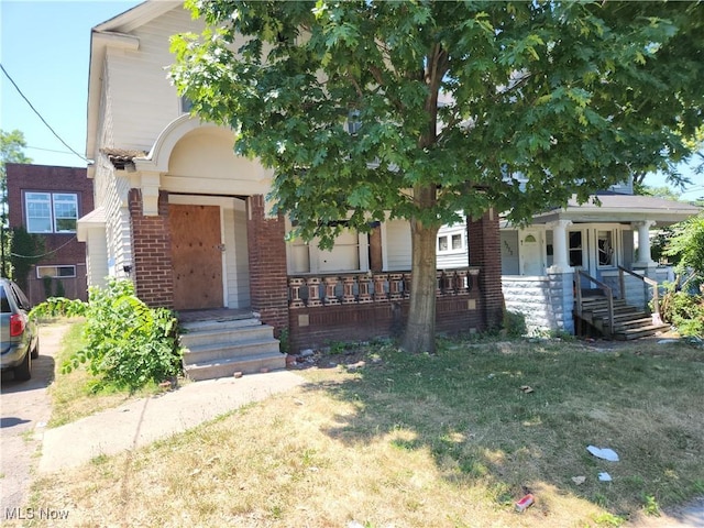 view of front of property with a porch, brick siding, and a front lawn