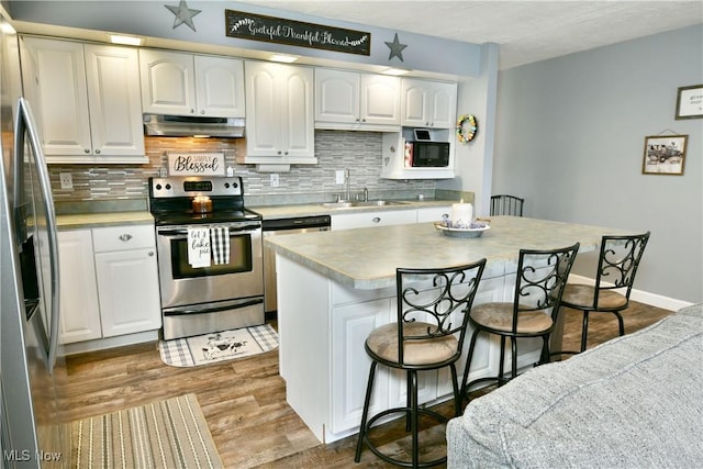 kitchen with a breakfast bar, wood finished floors, stainless steel appliances, under cabinet range hood, and a sink