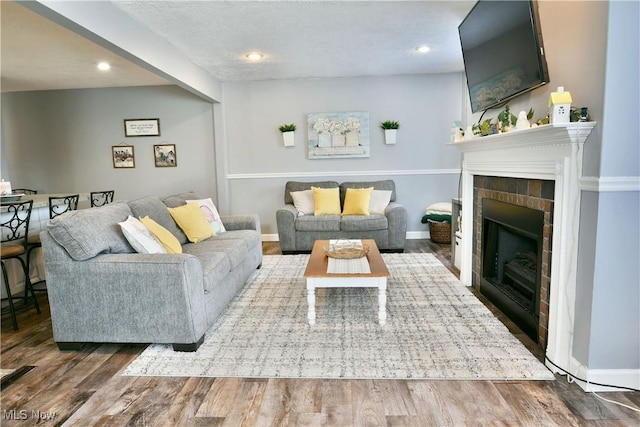 living area featuring recessed lighting, a fireplace, baseboards, and wood finished floors