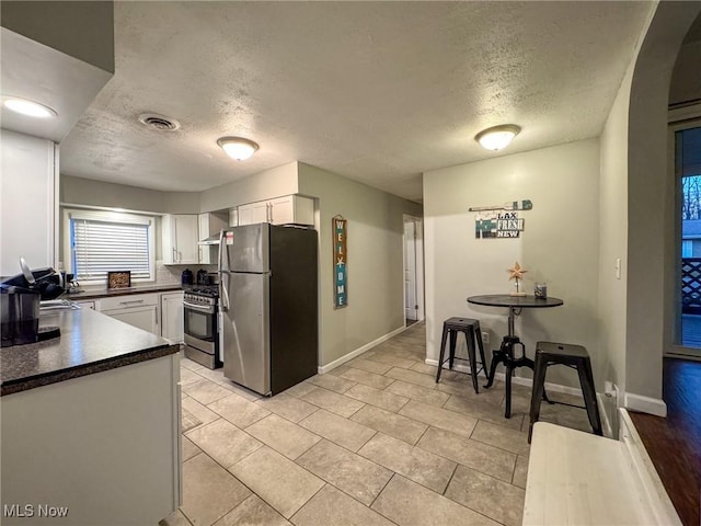 5192 University Dr, Geneva, OH 44041 - kitchen featuring stainless steel appliances, visible vents, white cabinets, wall chimney range hood, and dark countertops