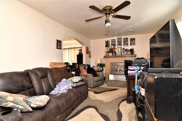 carpeted living area featuring arched walkways, a brick fireplace, and a ceiling fan