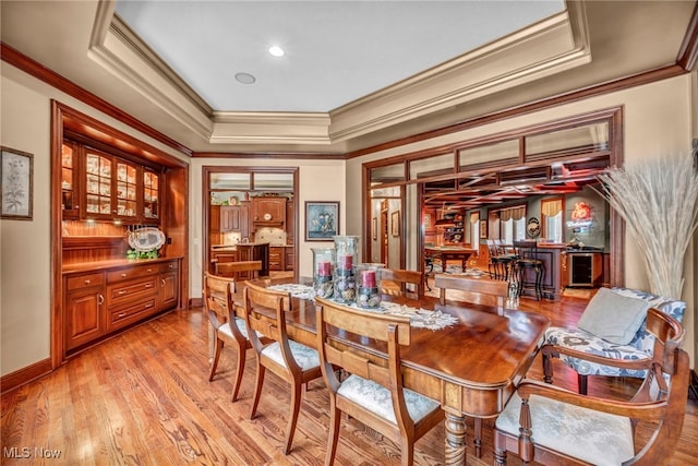 dining room with baseboards, a tray ceiling, light wood-style floors, and ornamental molding