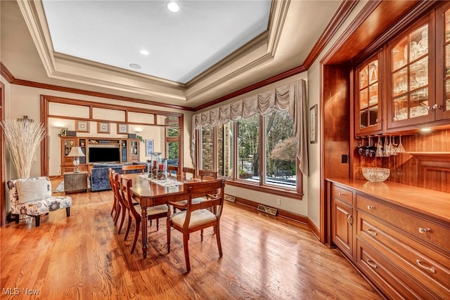 dining area featuring light wood-type flooring, a tray ceiling, baseboards, and visible vents