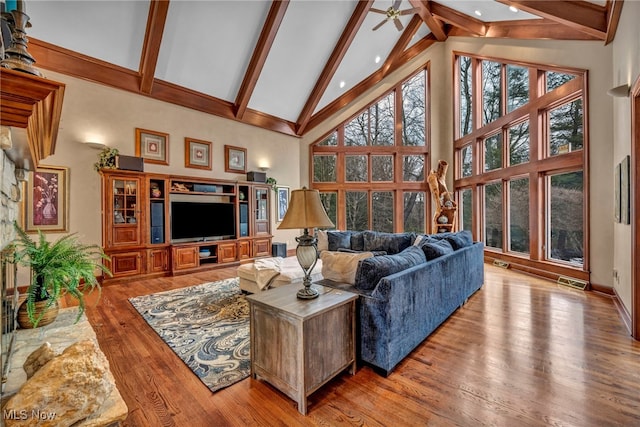 living room featuring visible vents, beam ceiling, high vaulted ceiling, a ceiling fan, and wood finished floors