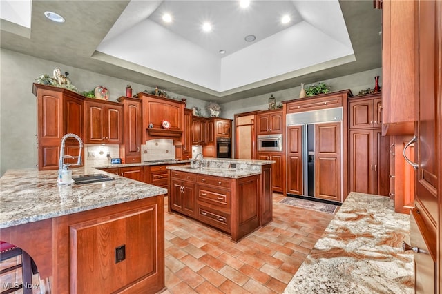 kitchen featuring a sink, a tray ceiling, light stone counters, and paneled refrigerator