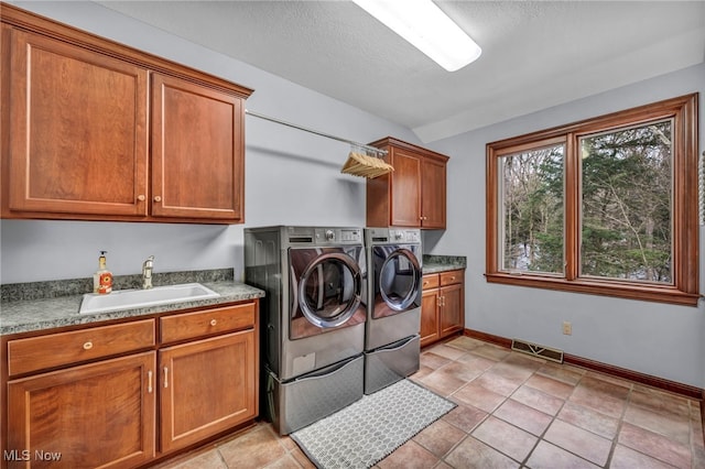 washroom featuring baseboards, visible vents, cabinet space, a sink, and washing machine and dryer