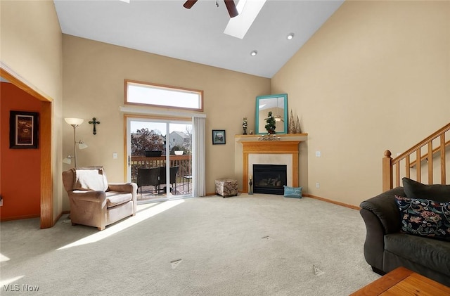 carpeted living area with a skylight, a fireplace, high vaulted ceiling, and a ceiling fan