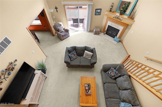 carpeted living area with a fireplace with flush hearth, stairs, visible vents, and baseboards