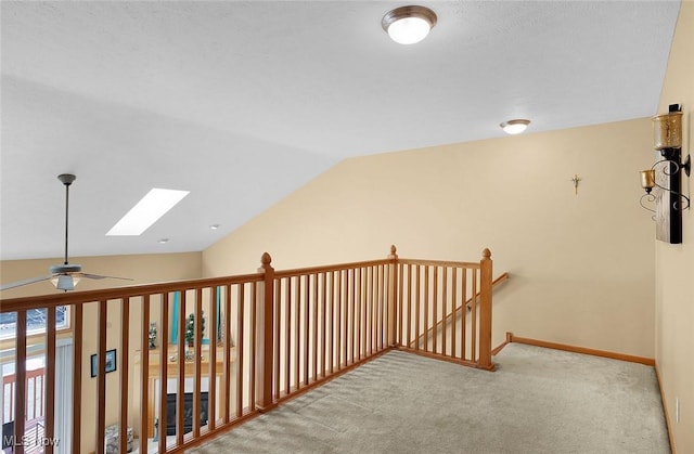 hallway featuring vaulted ceiling with skylight, carpet floors, an upstairs landing, and baseboards