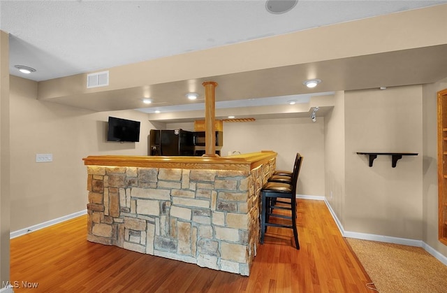 bar with a bar, visible vents, black fridge, and wood finished floors