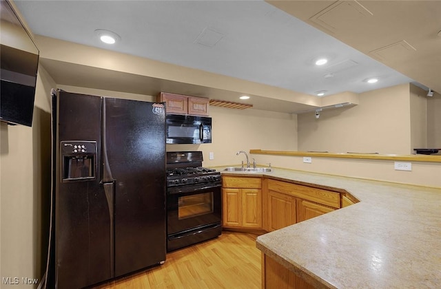 kitchen featuring a peninsula, a sink, light wood-style floors, light countertops, and black appliances