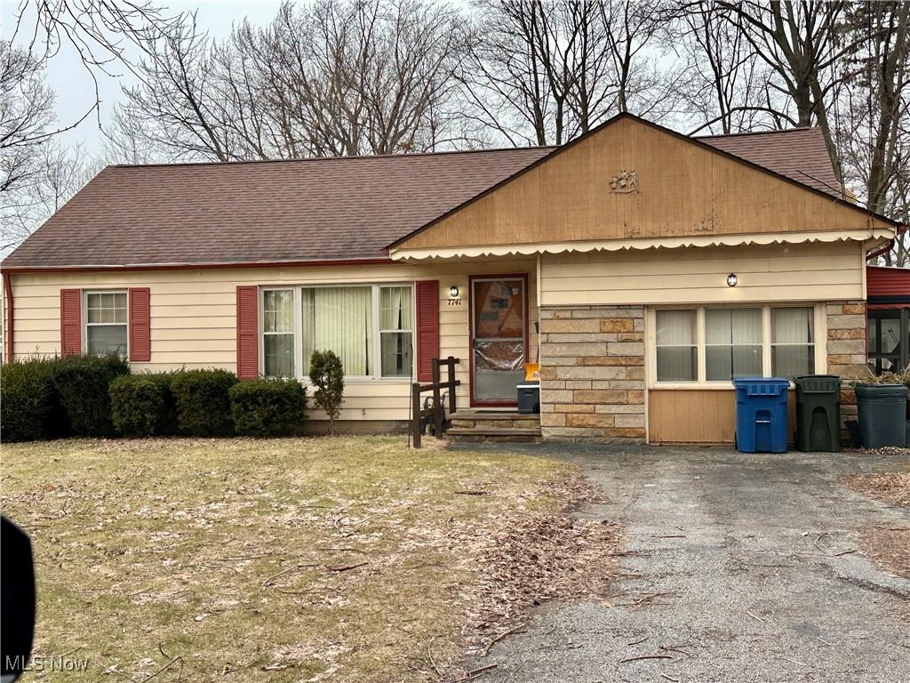 single story home featuring stone siding, roof with shingles, and driveway