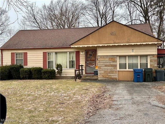 single story home featuring stone siding, roof with shingles, and driveway