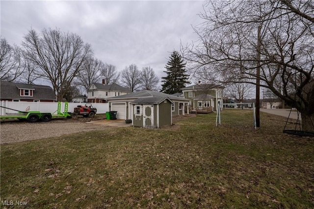 view of yard featuring an attached garage, driveway, an outdoor structure, and fence