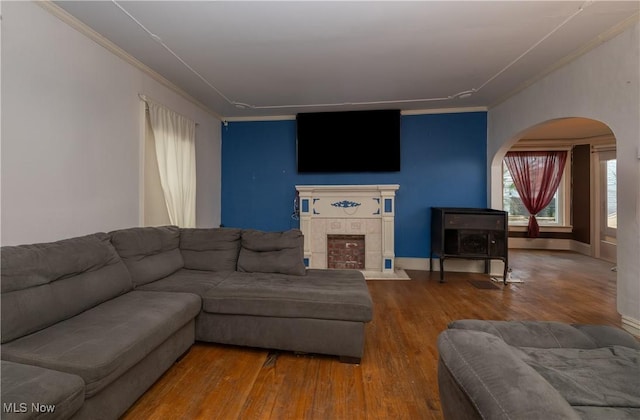 living room with crown molding, a tiled fireplace, baseboards, and wood finished floors