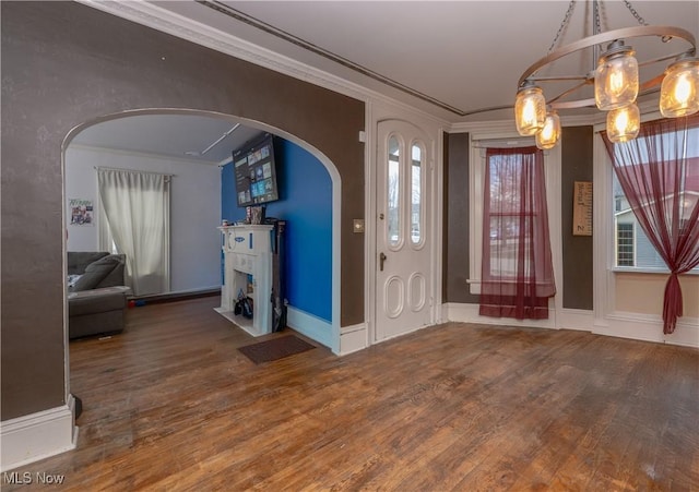 entryway with arched walkways, a fireplace, wood finished floors, and crown molding