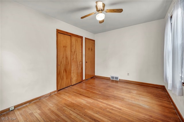 unfurnished bedroom with baseboards, light wood-style flooring, visible vents, and multiple closets