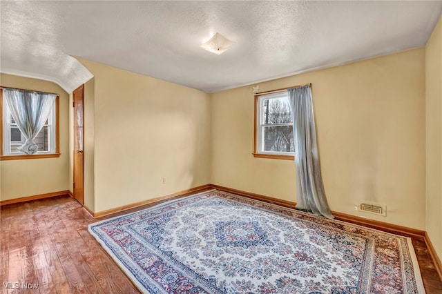 empty room with a textured ceiling, hardwood / wood-style floors, and baseboards