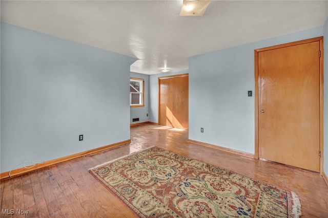 unfurnished room with wood-type flooring, visible vents, and baseboards