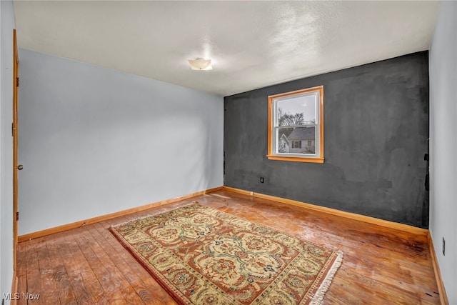 spare room featuring wood-type flooring and baseboards