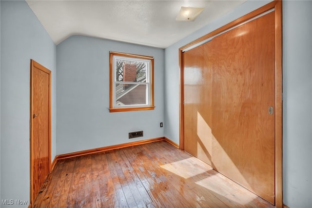 interior space with a closet, visible vents, hardwood / wood-style floors, vaulted ceiling, and baseboards