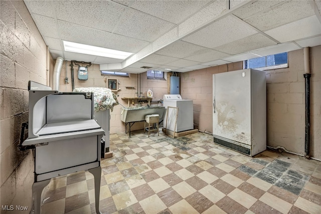 basement with freestanding refrigerator, concrete block wall, washer / dryer, and tile patterned floors