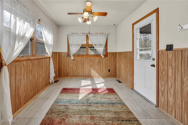 interior space with visible vents, wainscoting, ceiling fan, tile patterned floors, and wood walls