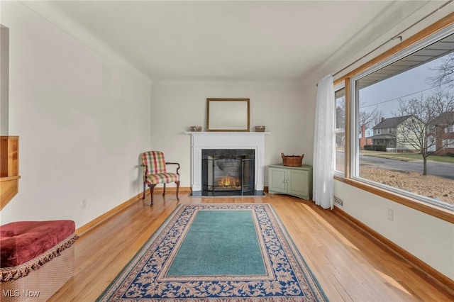 living area featuring a fireplace with flush hearth, baseboards, and wood finished floors