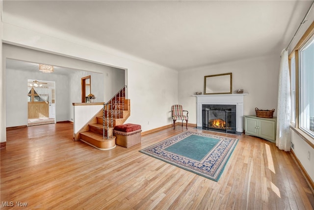 living room with a warm lit fireplace, stairway, hardwood / wood-style flooring, and baseboards