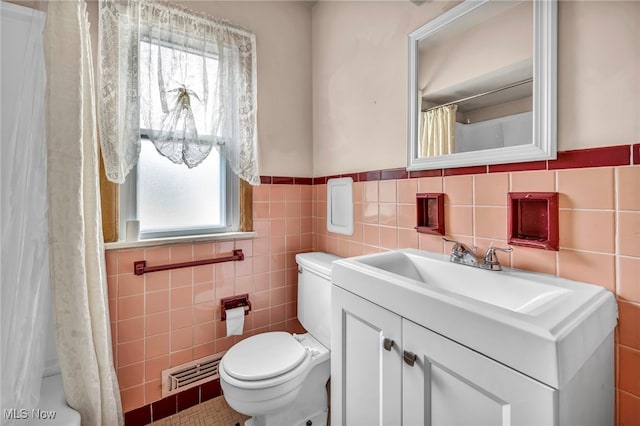 bathroom featuring visible vents, wainscoting, toilet, vanity, and tile walls