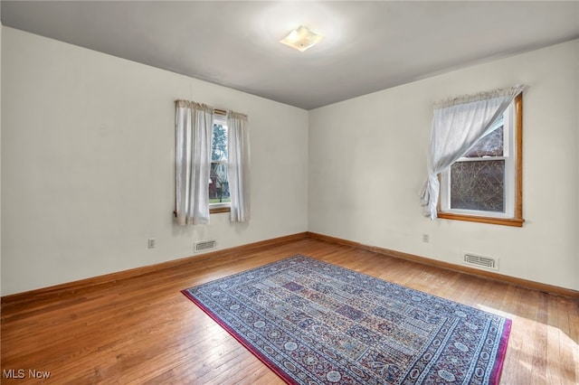 spare room with hardwood / wood-style flooring, visible vents, and baseboards