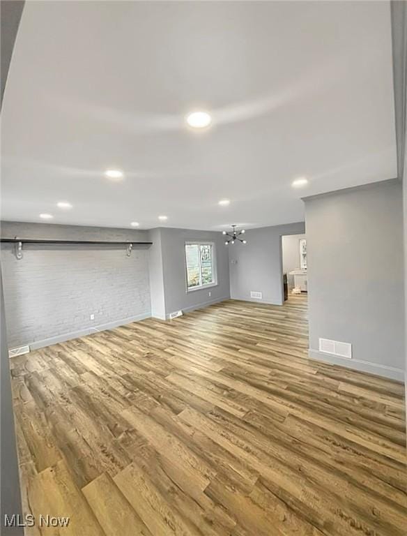 unfurnished living room featuring baseboards, visible vents, brick wall, wood finished floors, and an inviting chandelier